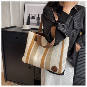 Detail of striped canvas tote bag with brown straps and leather logo patch on a model