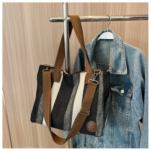 Detail of striped canvas tote bag featuring brown leather logo and wide woven straps