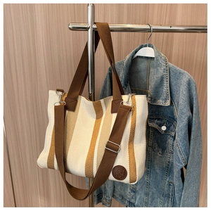 Close-up of striped canvas tote bag detail with circular leather logo and shoulder strap
