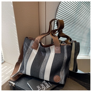 Macro detail of striped canvas tote bag featuring brown woven handles and leather logo patch
