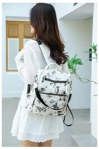 Rear view of a model wearing a white butterfly print backpack with tassel zipper detail