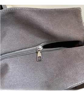 Detailed close-up of the smooth metal zipper and gray canvas texture on the tote bag
