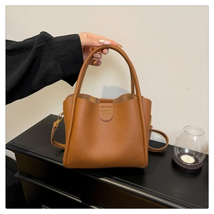 Détail du sac seau en cuir marron avec ferrures dorées et logo sur surface en bois