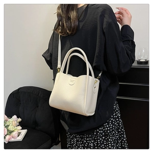 Vue latérale du sac seau en cuir crème porté par un mannequin avec bandoulière