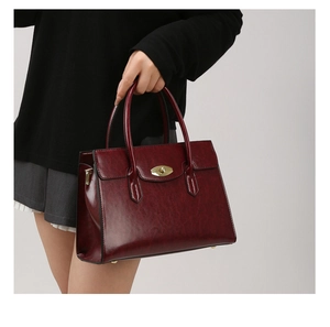 Detail of burgundy leather tote bag featuring a gold twist-lock and textured finish
