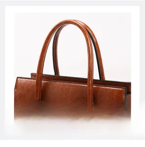 Detail shot of sturdy double handles and oil-edge finish on a brown leather handbag