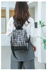 Plaid backpack with black leather trim and gold zippers shown on a model in city setting