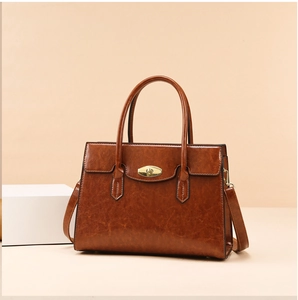 Detail of caramel leather tote bag showing gold twist-lock hardware and textured surface