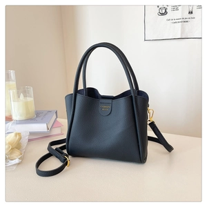 Détail du sac seau en cuir grainé noir avec finitions dorées et texte de mode