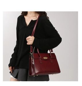 Side view of wine red leather handbag with gold twist lock on minimalist gray studio background