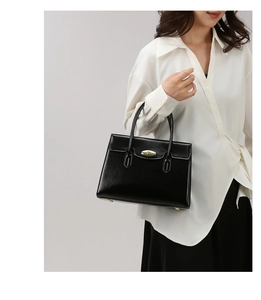 Close-up of black glossy leather handbag with elegant gold oval twist lock closure