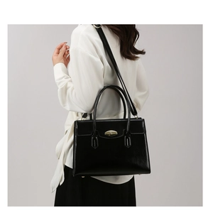 Detailed view of black oil leather handbag with golden twist lock and precise stitching
