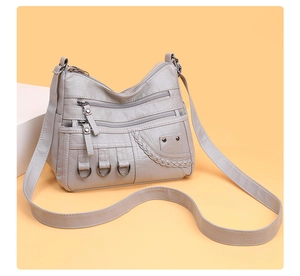 Detail of grey woven shoulder bag showing three parallel zipper pockets and metal D-rings