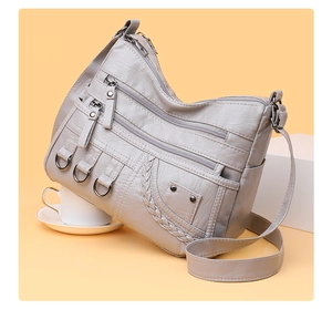 Macro detail of multi-zipper compartments and textured leather on a grey shoulder bag