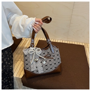 Detail of checkered bucket bag featuring lace bow, pearls, and heart charm accents