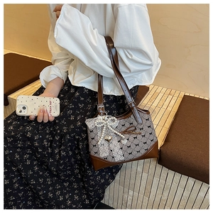 Detail of retro bow print bucket bag with lace trim and elegant pearl pendant accessory
