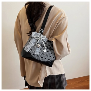 Detail view of bow patterns and pearl charms on a black and white checkered bucket bag