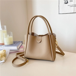 Sac seau beige tendance avec logo doré et bandoulière réglable sur surface blanche
