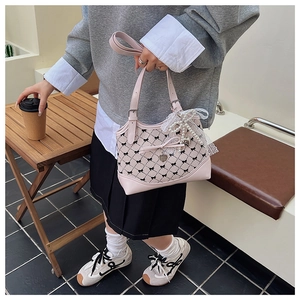 Detail of pink bow-patterned bucket bag with lace trim and heart pearl charm in hand