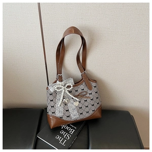 Close-up of brown leather bag with plaid fabric, lace bow, and pearl heart charm