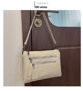 Detail view of off-white multi-zipper handbag with vintage leather texture hanging on a door