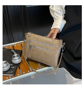 Detail view of beige multi-zippered crossbody bag on a wooden bench with lifestyle props