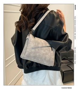 Detail of light gray crossbody bag showing refined leather texture and metal zipper detail