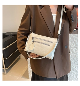 Détail du sac bandoulière blanc montrant la texture cuir litchi et double poches zippées