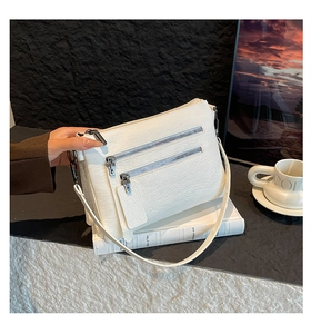 Close-up of white lychee leather shoulder bag with triple silver zippers on white books
