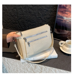 Detail of creamy white PU leather shoulder bag with multiple silver zipper pockets