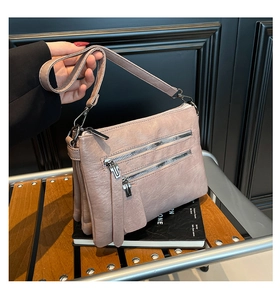 Detail of dusty rose crossbody bag with multi-layer zippers and soft pebbled texture