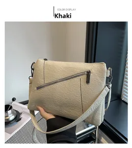 Close-up of khaki pebbled leather crossbody bag with decorative zipper and metal hardware