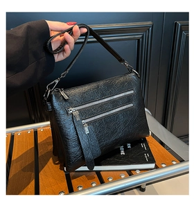 Detail of black lychee grain leather handbag featuring dual front silver zipper pockets