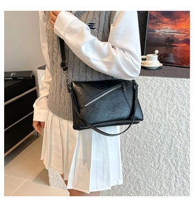 Detail of minimalist black leather crossbody bag with silver decorative zipper and strap