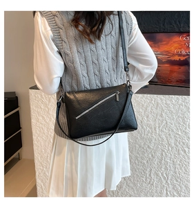 Detail of minimalist black crossbody bag with metallic zipper and textured leather finish
