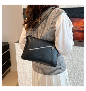 Detail view of the black pleated leather shoulder bag with diagonal zipper pocket on a model