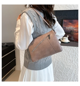 Detailed view of a taupe textured faux leather crossbody bag worn by a model in a room