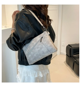 Rear view of a textured grey crossbody bag with a zipper pocket on the back worn by model
