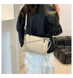 Close-up of a beige crossbody bag on a model showing litchi grain texture and pockets