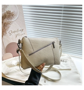 Detail of cream white faux leather crossbody bag with textured pebble finish and diagonal zip
