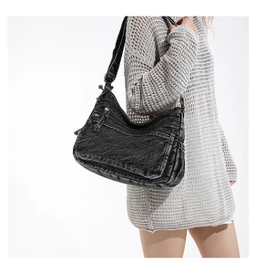 Detail of a large black washed denim crossbody bag featuring multiple zipper pockets