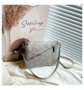 Detailed close-up of grey leather crossbody bag with metal zippers on white fabric