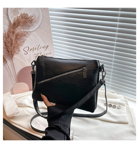 Detail of black pebble leather crossbody bag featuring silver side buckles and zipper
