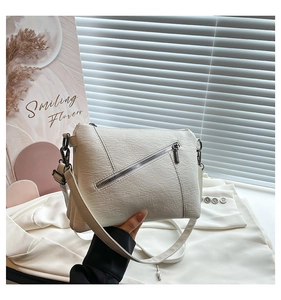 Detail of white textured leather crossbody bag with diagonal zipper and dark metal hardware