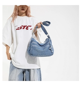 Detail of light blue denim hobo bag featuring double front zippers and woven knot pulls