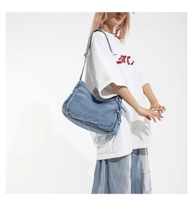 Close-up of washed blue denim shoulder bag featuring utility multi-pocket design