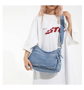 Close-up of blue washed denim crossbody bag featuring tassel zippers and side pockets