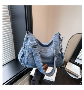 Detail of blue denim shoulder bag showing multiple zipper pockets and metal hardware