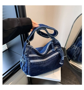 Detail of blue denim shoulder bag showing washed texture, multi-zipper pockets and tassels