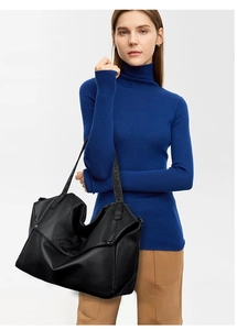 Detail of a large black leather tote bag with litchi texture on a female model shoulder